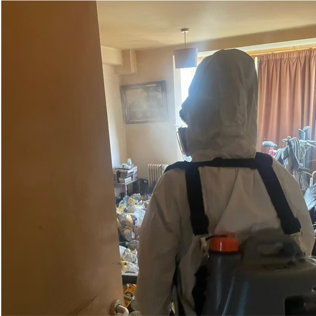 Cleaner in messy room wearing white hazard suit